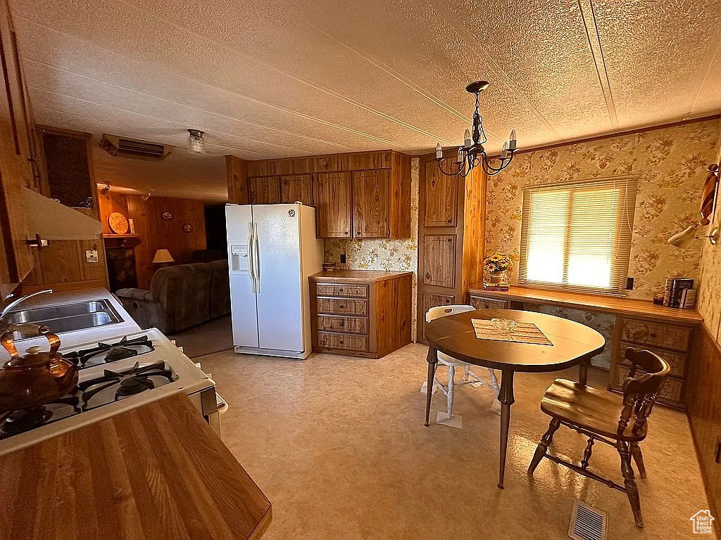 Kitchen with white appliances, wallpapered walls, visible vents, brown cabinets, and a sink