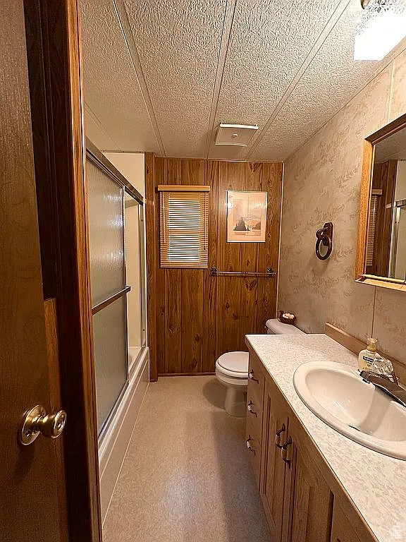 Full bathroom with toilet, a shower with shower door, a textured ceiling, vanity, and wood walls