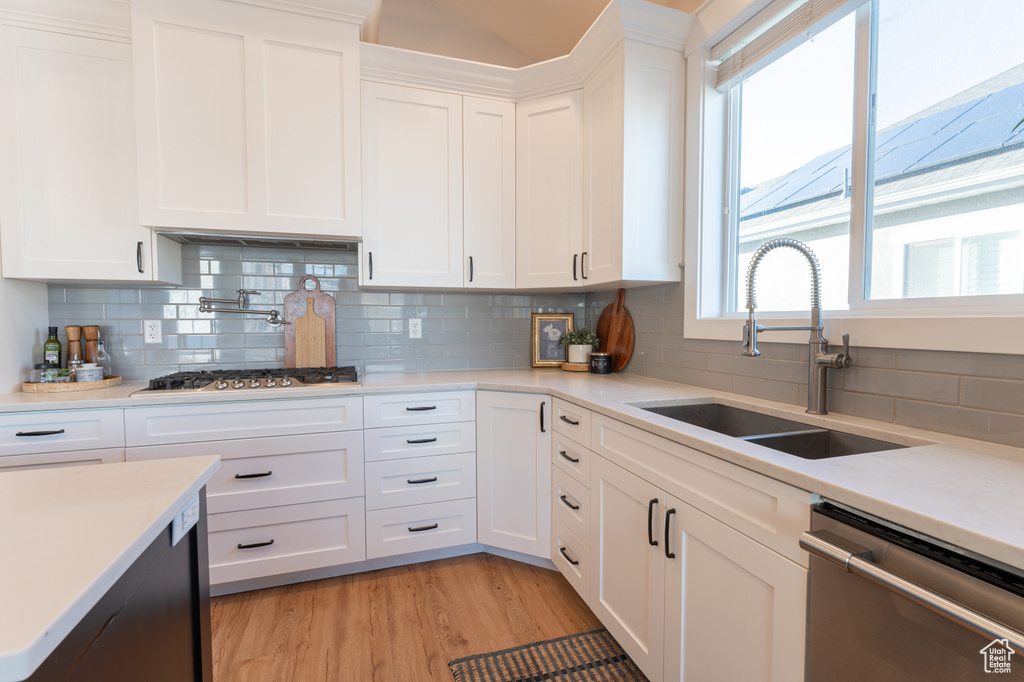 Kitchen with stainless steel appliances, light countertops, light wood-style flooring, white cabinetry, and a sink