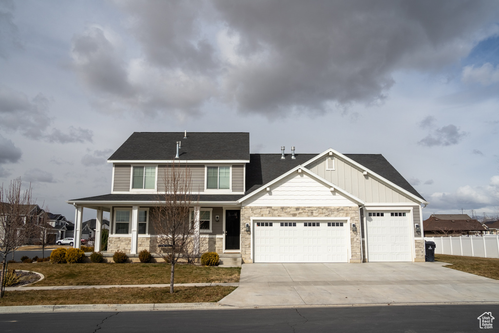Craftsman-style house featuring board and batten siding, fence, a garage, stone siding, and driveway