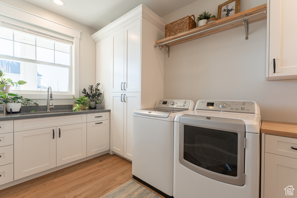 Clothes washing area with cabinet space, light wood finished floors, independent washer and dryer, a sink, and recessed lighting