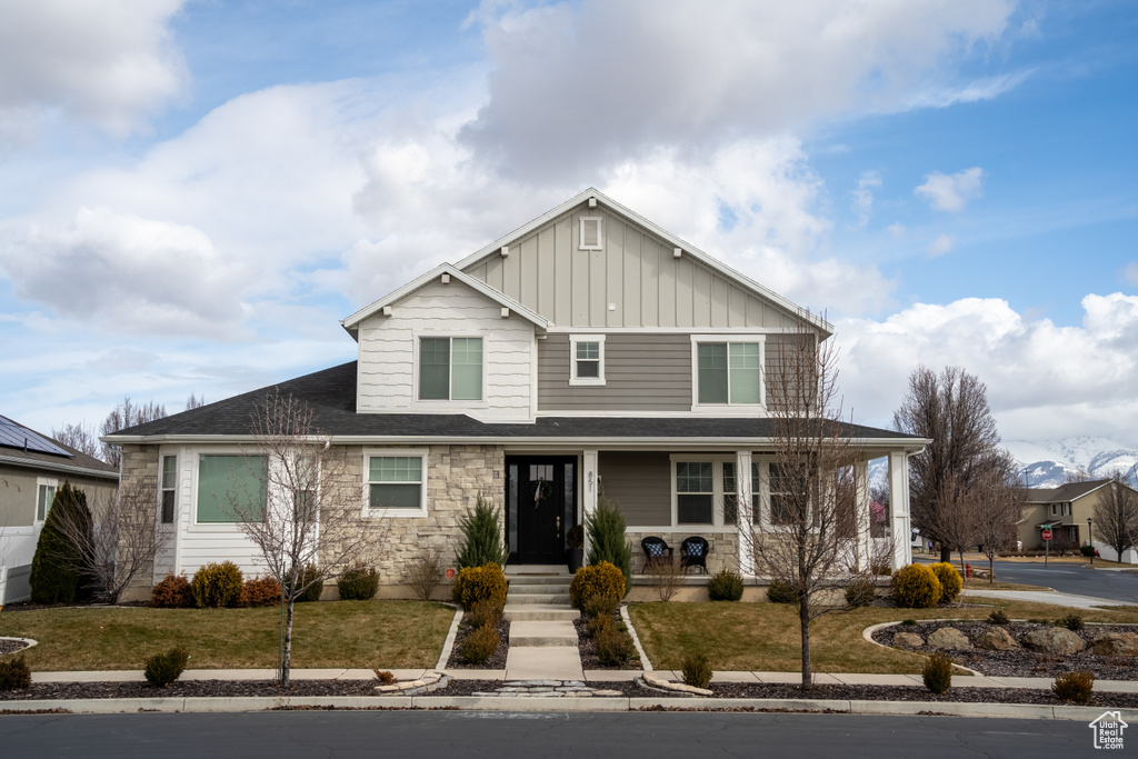 View of front facade featuring covered porch, stone siding, a front lawn, and board and batten siding