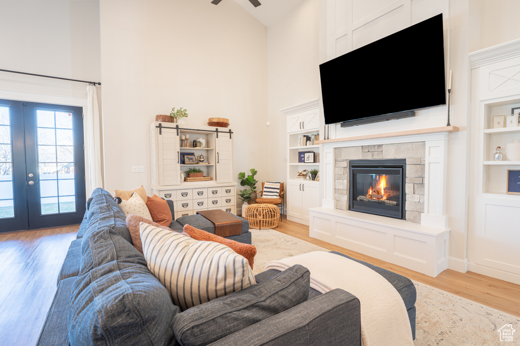 Living room featuring built in features, french doors, light wood-style floors, a stone fireplace, and high vaulted ceiling