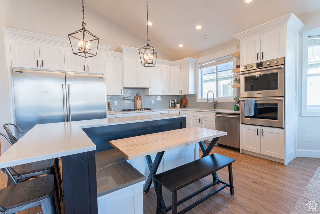 Kitchen featuring lofted ceiling, stainless steel appliances, a sink, white cabinetry, and tasteful backsplash
