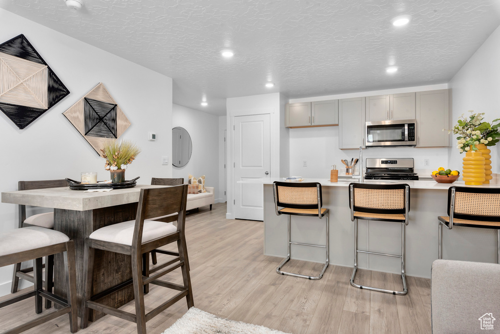 Kitchen with stainless steel appliances, light countertops, gray cabinetry, light wood-type flooring, and a kitchen bar