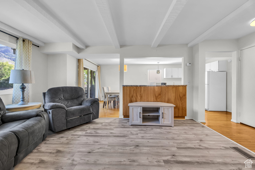 Living area with light wood-style floors, visible vents, and beam ceiling