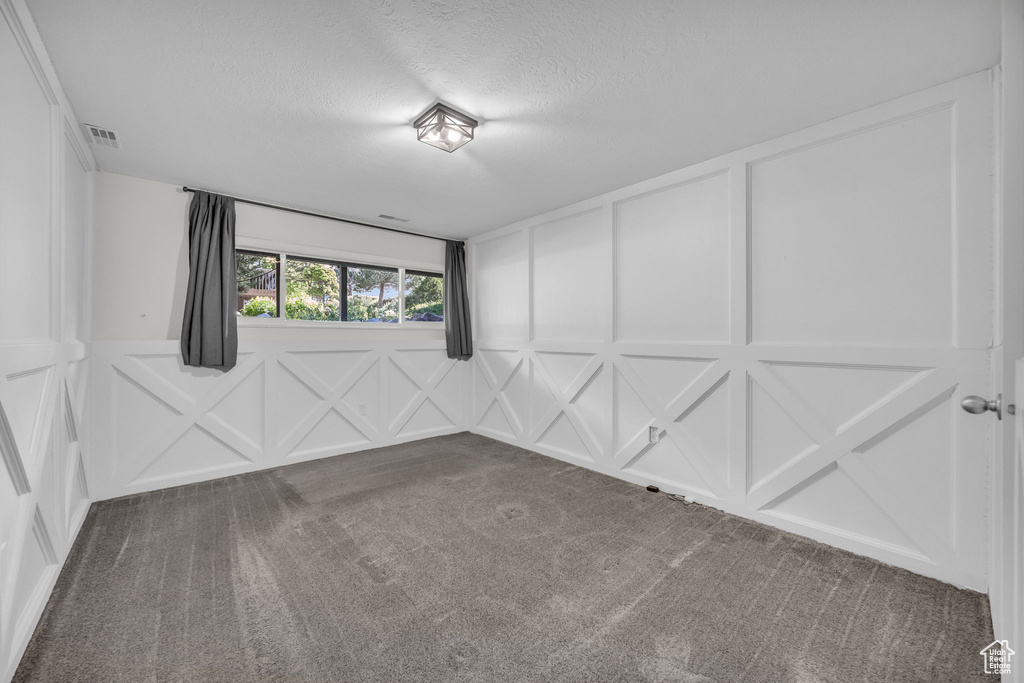Carpeted empty room with a textured ceiling, a decorative wall, and visible vents