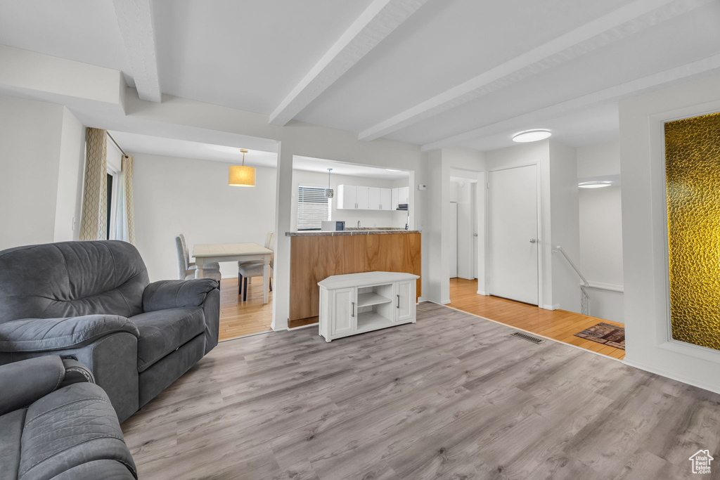 Living area with light wood-style floors, visible vents, and beam ceiling