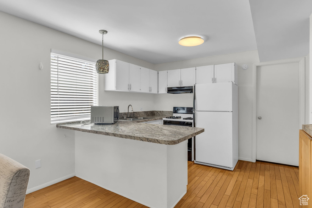 Kitchen featuring a sink, a peninsula, stainless steel microwave, freestanding refrigerator, and under cabinet range hood