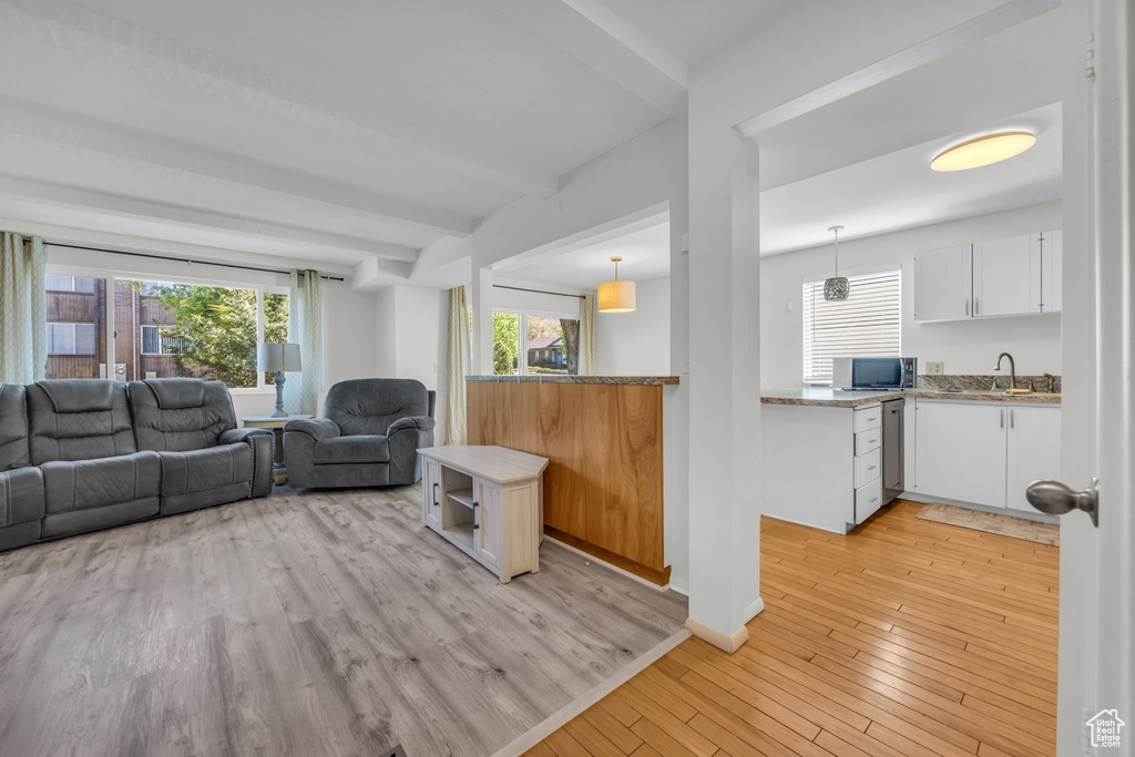 Living room featuring beamed ceiling, light wood finished floors, and plenty of natural light