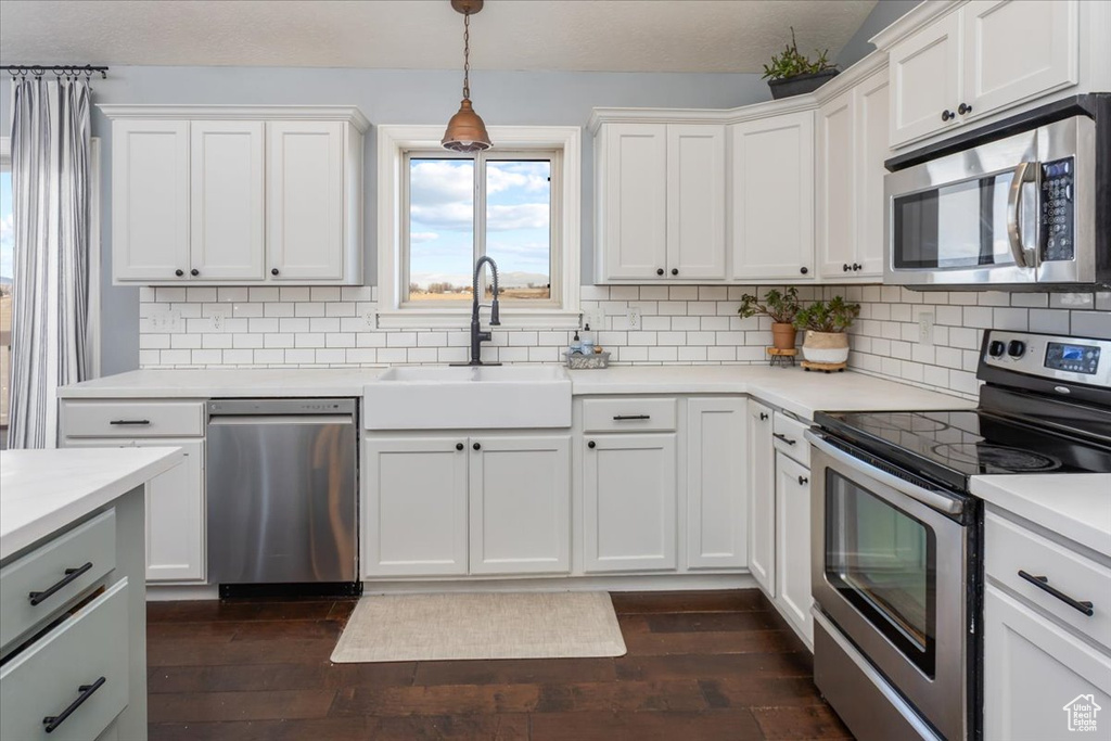 Kitchen featuring stainless steel appliances, light countertops, dark wood-type flooring, white cabinetry, and a sink