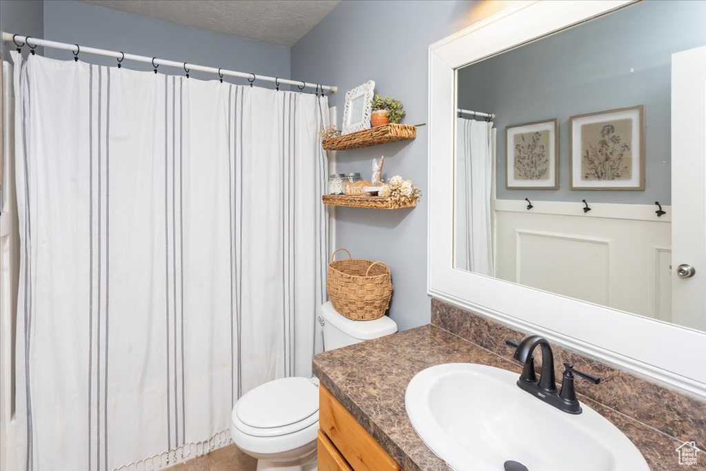 Bathroom featuring a shower with shower curtain, a textured ceiling, toilet, and vanity