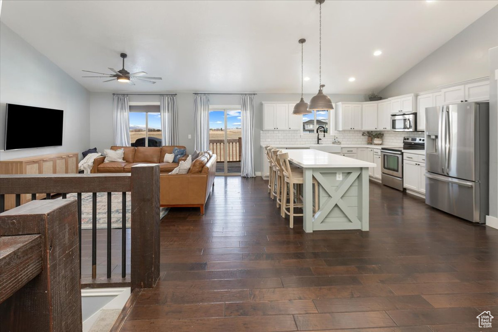 Kitchen featuring stainless steel appliances, lofted ceiling, light countertops, and dark wood-style floors