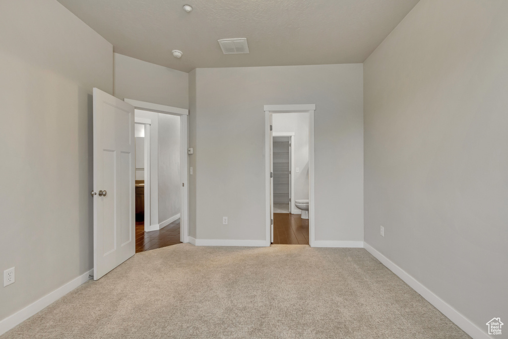 Unfurnished bedroom featuring carpet floors, visible vents, connected bathroom, and baseboards