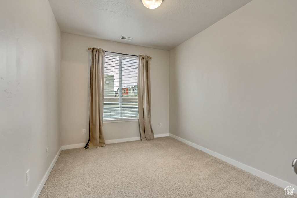 Spare room featuring light carpet, a textured ceiling, visible vents, and baseboards