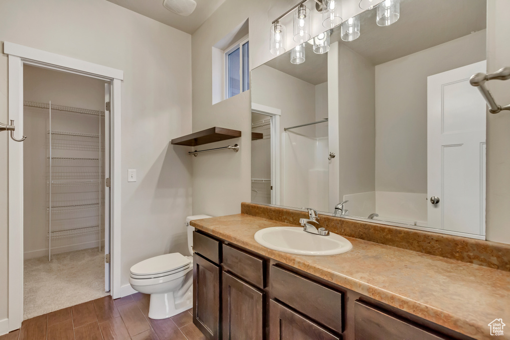 Full bath with baseboards, toilet, vanity, a walk in closet, and wood finish floors