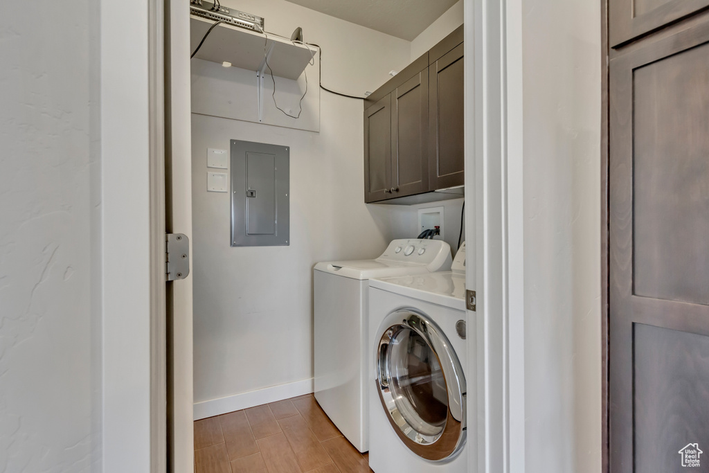 Laundry room with baseboards, light wood-type flooring, independent washer and dryer, cabinet space, and electric panel