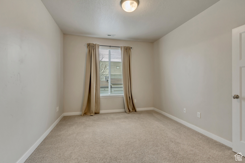 Spare room with light colored carpet, visible vents, baseboards, and a textured ceiling