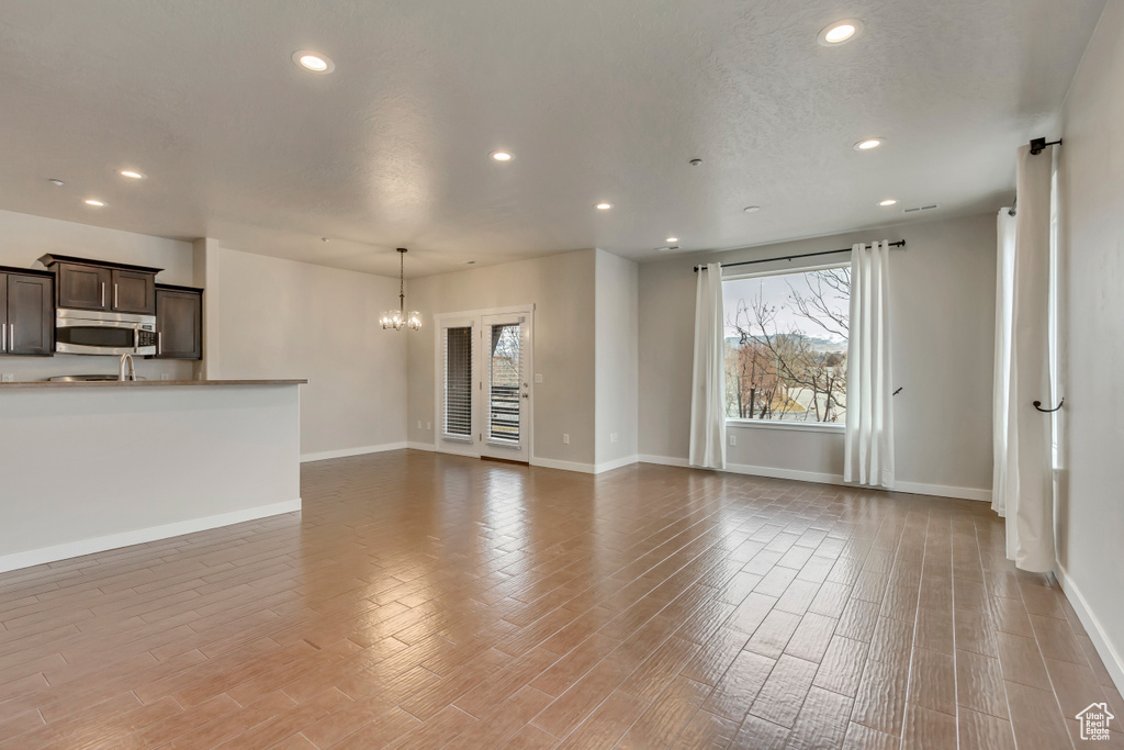 Unfurnished living room with a chandelier, recessed lighting, light wood-style flooring, and baseboards