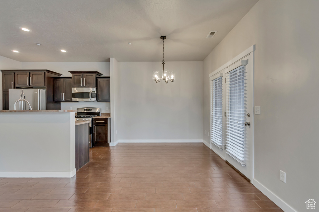Kitchen with dark brown cabinetry, visible vents, baseboards, stainless steel appliances, and a chandelier