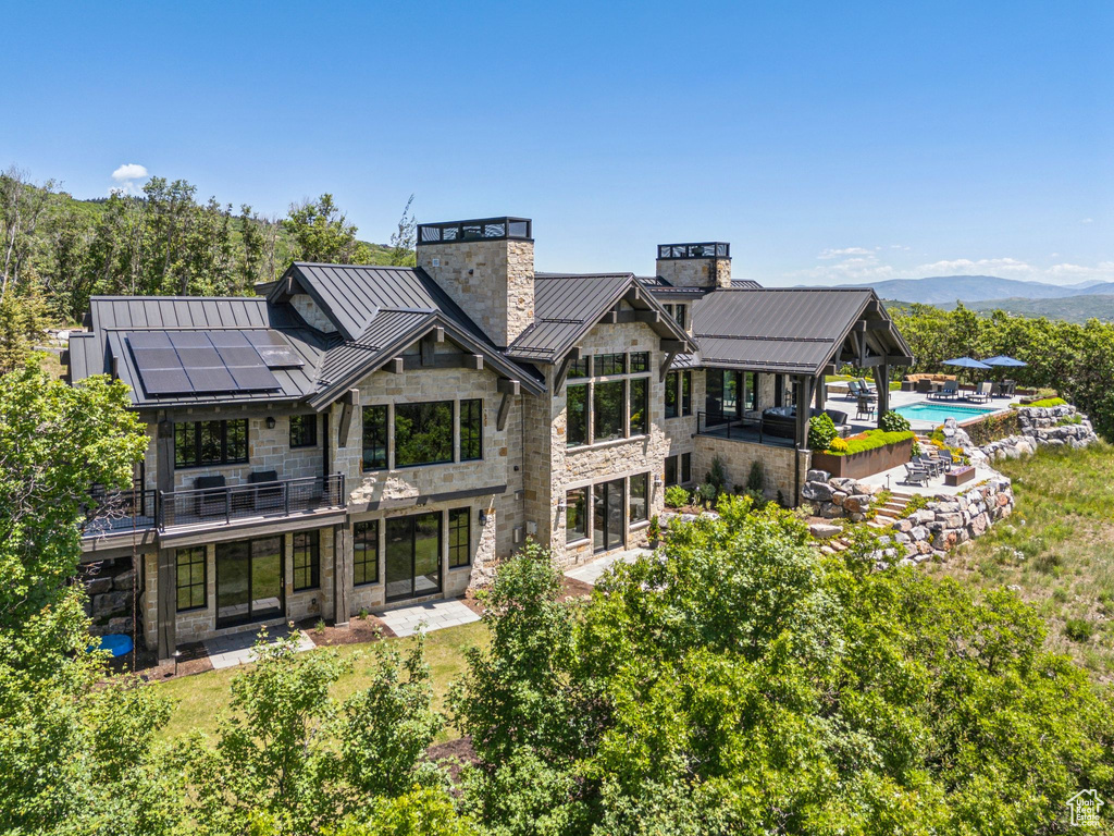 Back of property with a standing seam roof, a chimney, roof mounted solar panels, a metal roof, and stone siding