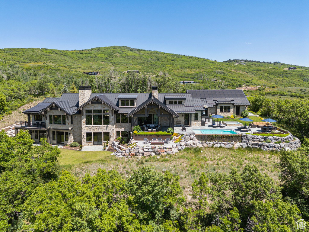 Rear view of house featuring a chimney, a standing seam roof, stone siding, and an outdoor pool
