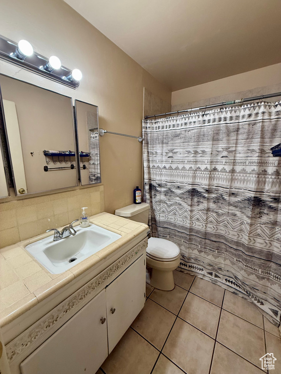 Bathroom featuring tasteful backsplash, a shower with shower curtain, toilet, tile patterned flooring, and vanity