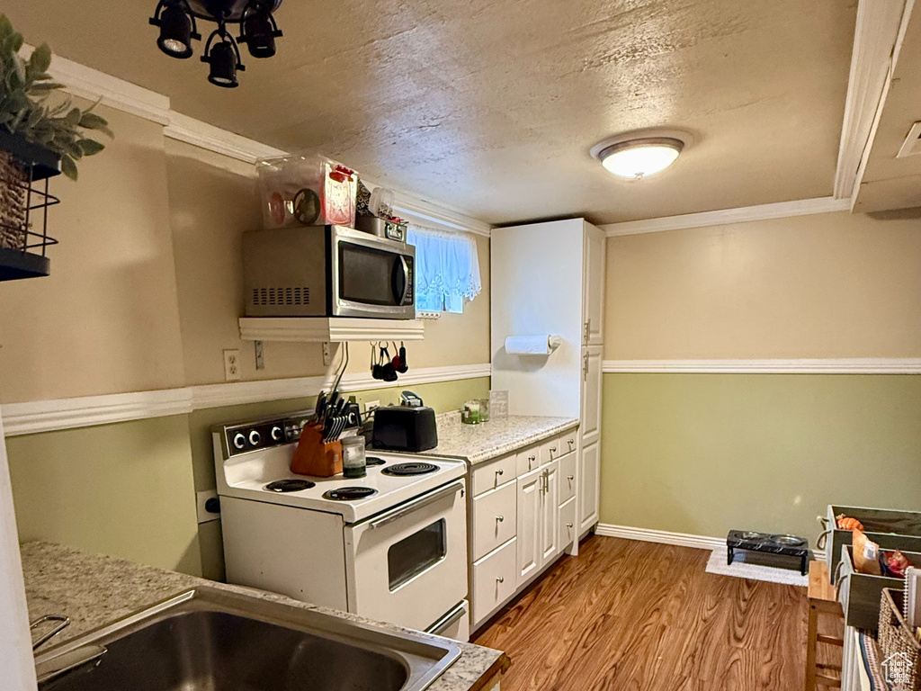 Kitchen featuring white range with electric cooktop, a sink, white cabinetry, light wood finished floors, and stainless steel microwave