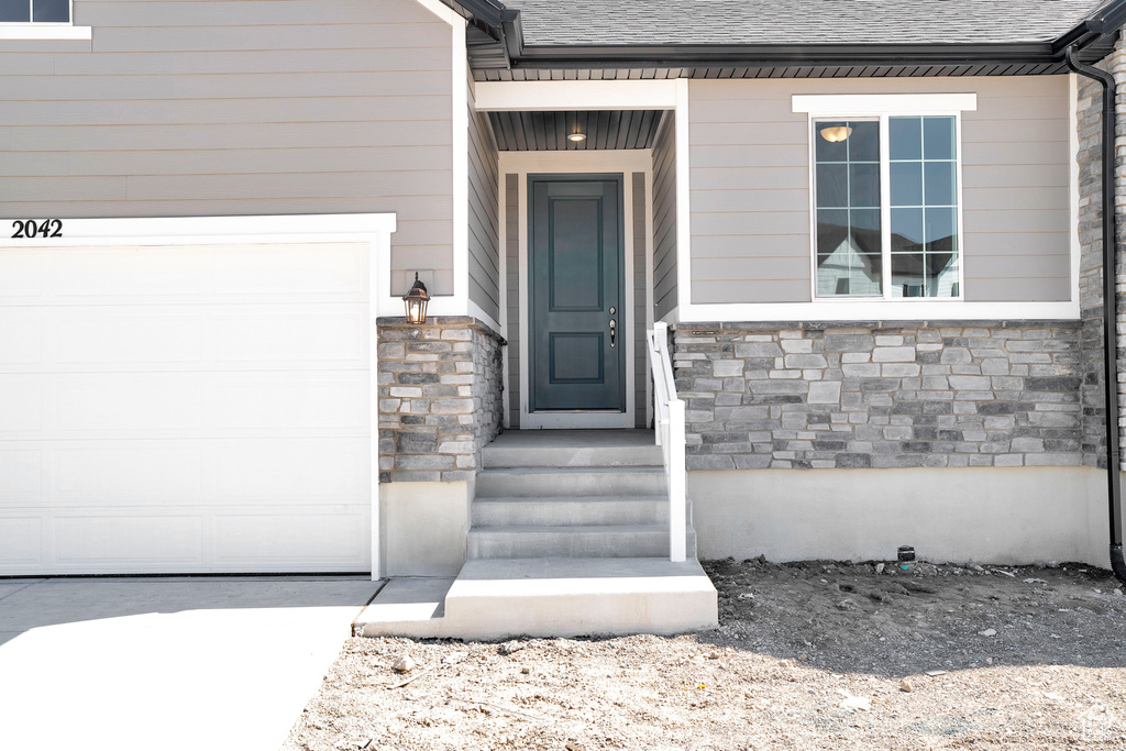 View of exterior entry featuring roof with shingles and stone siding