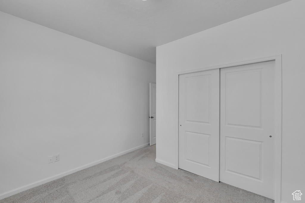 Unfurnished bedroom featuring a closet, baseboards, and light colored carpet