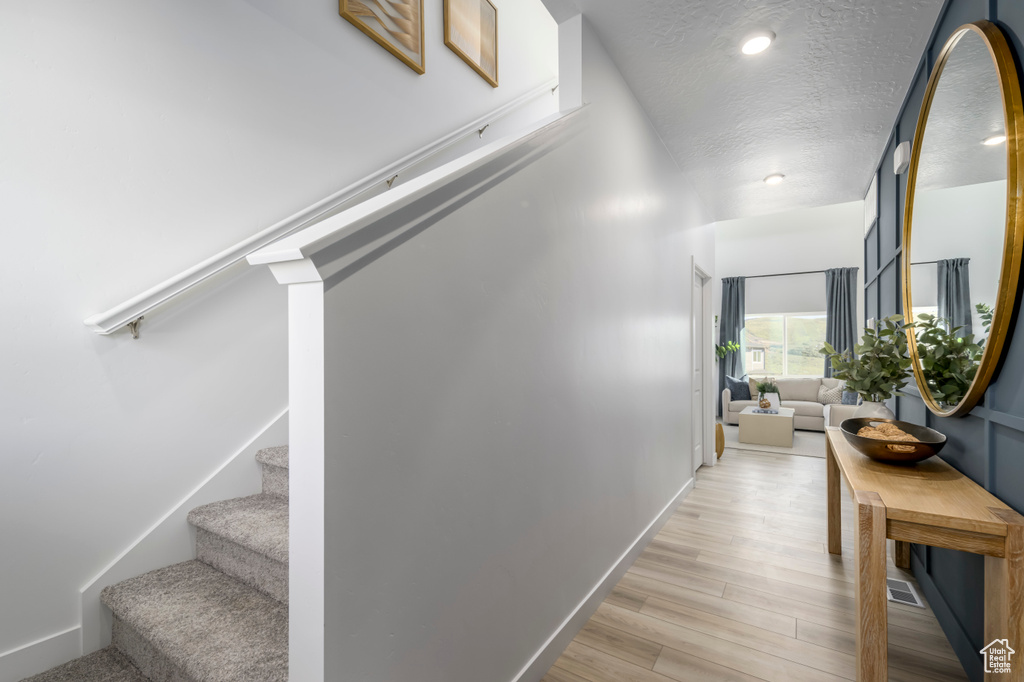 Hallway featuring light wood-type flooring, stairs, baseboards, and a textured ceiling