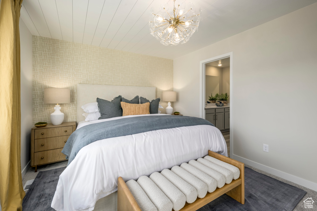 Bedroom with baseboards, wooden ceiling, an accent wall, ensuite bathroom, and a notable chandelier