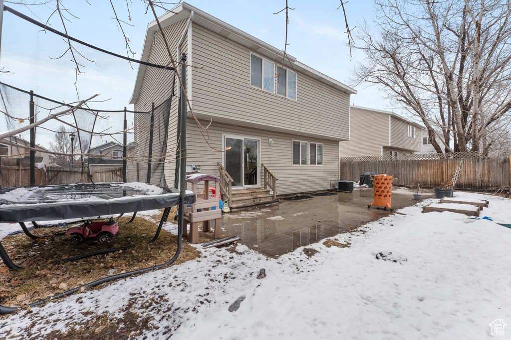 Snow covered rear of property featuring entry steps, a patio, a fenced backyard, a trampoline, and cooling unit