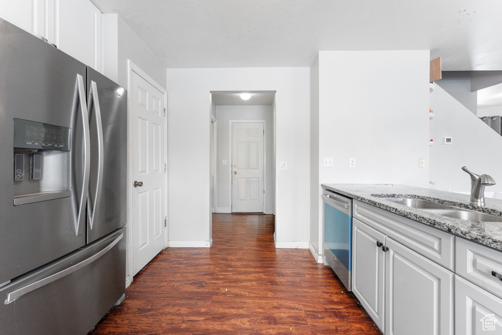 Kitchen featuring a sink, white cabinets, appliances with stainless steel finishes, light stone countertops, and dark wood finished floors