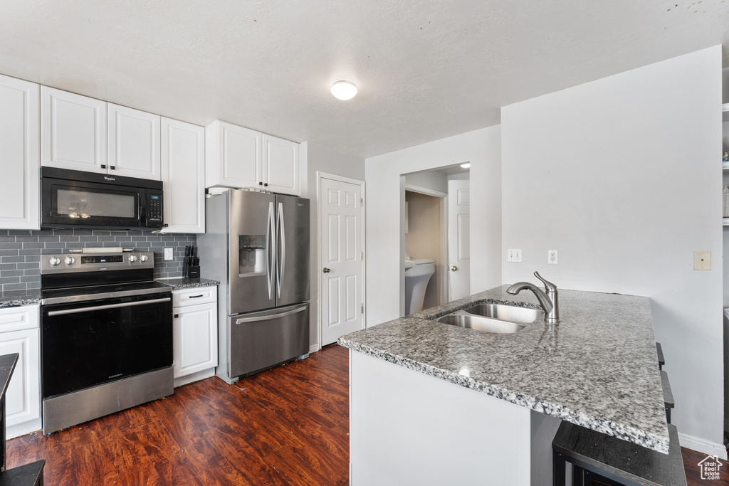 Kitchen with light stone counters, dark wood-style floors, stainless steel appliances, decorative backsplash, and a sink