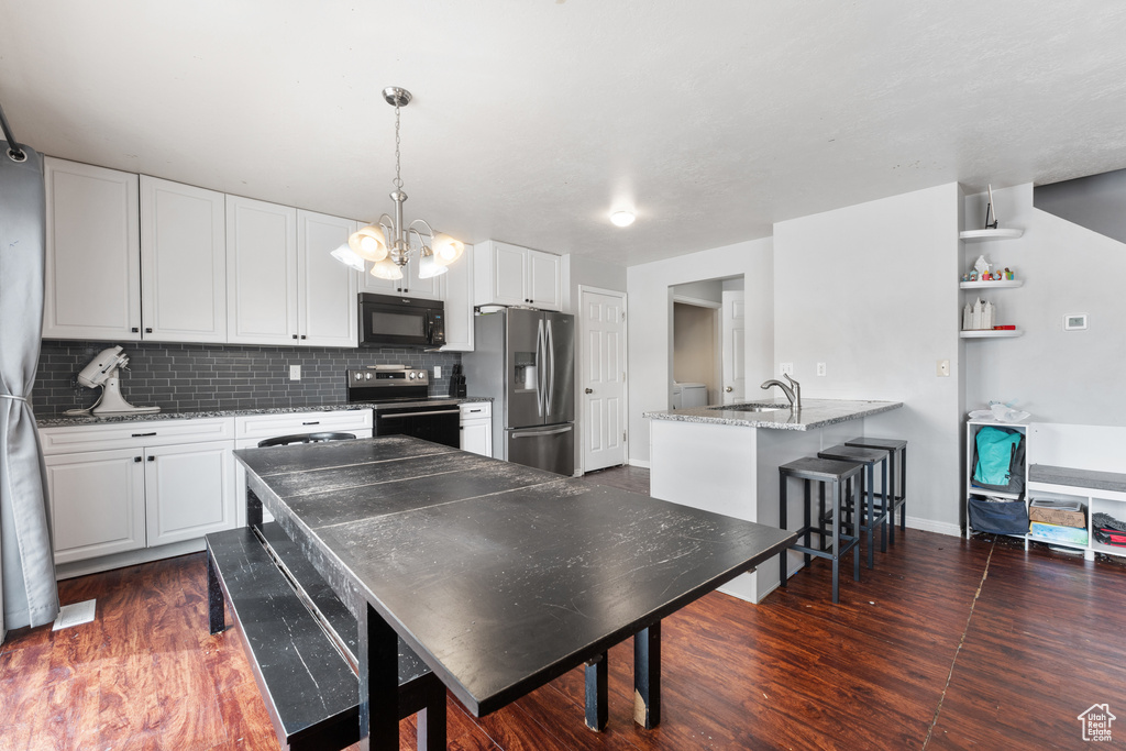 Kitchen with dark wood finished floors, a peninsula, stainless steel appliances, white cabinetry, and backsplash