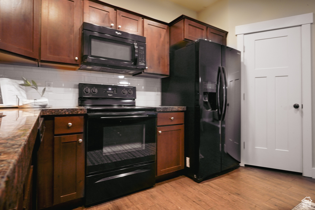 Kitchen with black appliances, light wood-type flooring, and tasteful backsplash