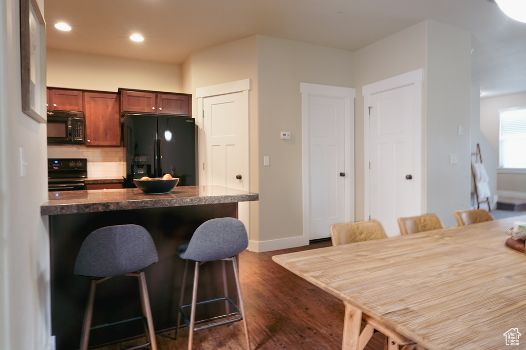 Kitchen featuring black appliances, a breakfast bar, backsplash, dark wood finished floors, and dark countertops