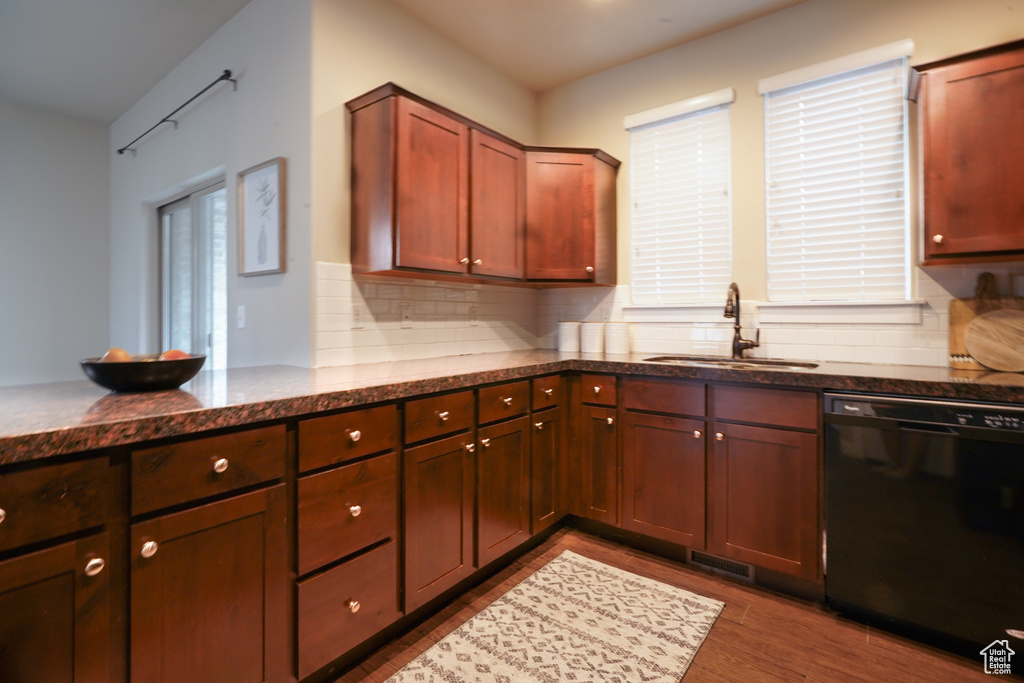 Kitchen featuring black dishwasher, tasteful backsplash, dark wood finished floors, dark stone counters, and a peninsula