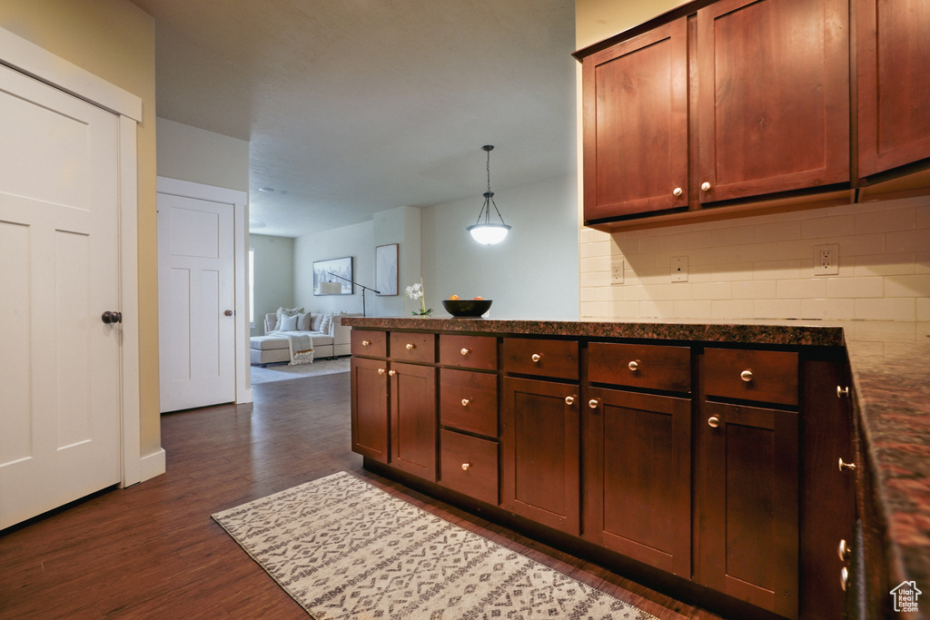 Kitchen featuring dark wood finished floors, open floor plan, a peninsula, hanging light fixtures, and dark stone countertops
