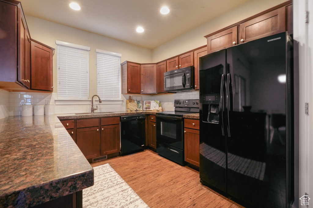 Kitchen featuring black appliances, light wood-type flooring, tasteful backsplash, recessed lighting, and dark countertops