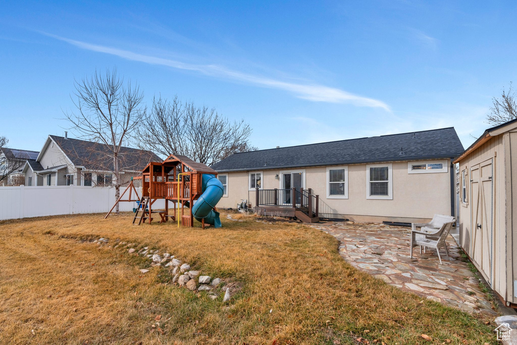 Back of property featuring a lawn, fence, a patio area, a playground, and stucco siding