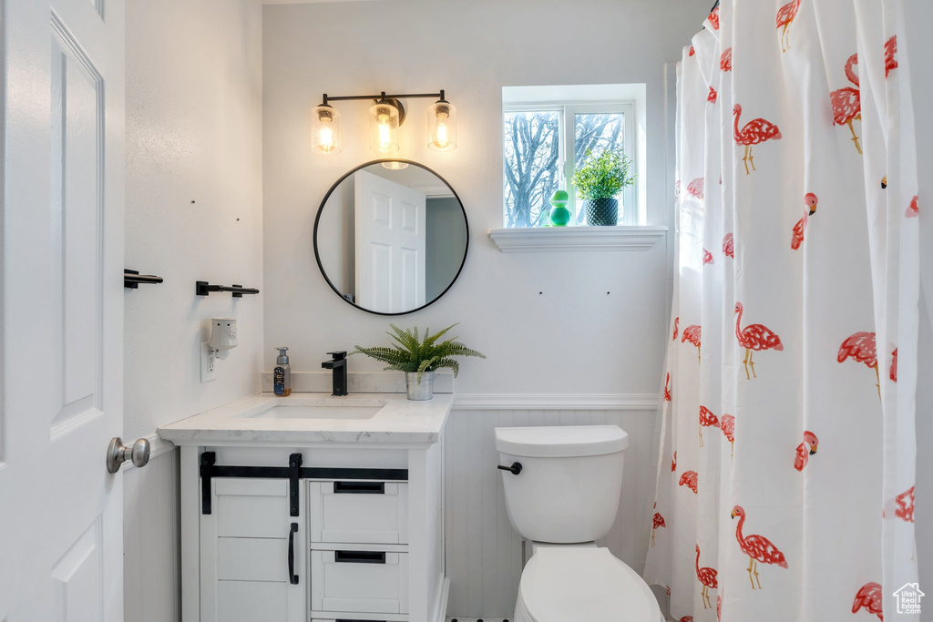 Bathroom with a shower with curtain, wainscoting, vanity, and toilet