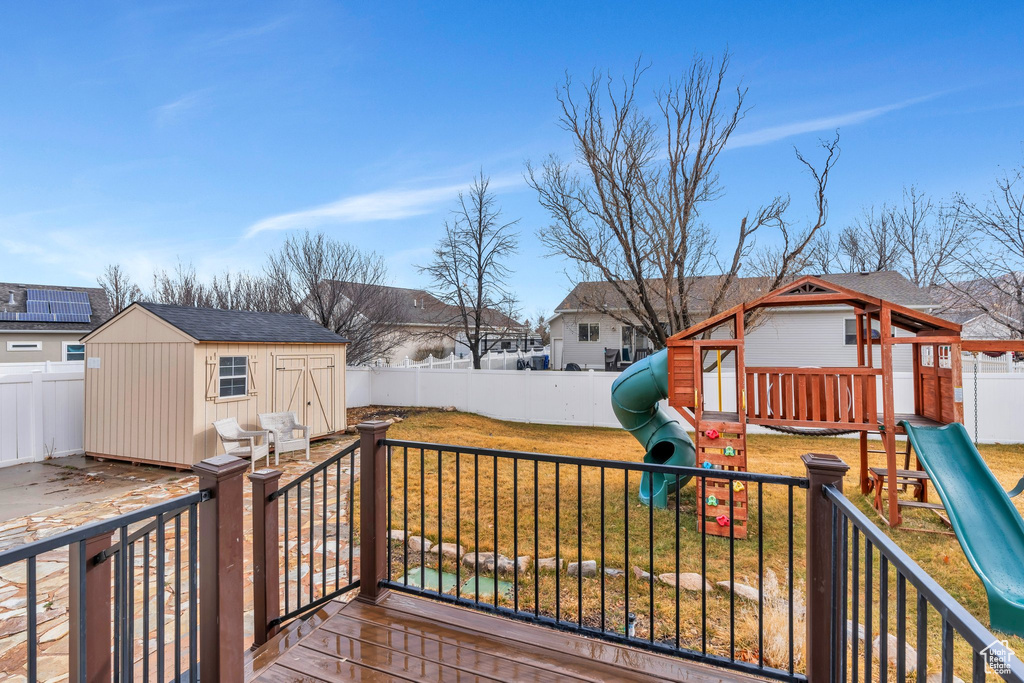 Wooden terrace featuring a shed, an outdoor structure, a playground, and a yard