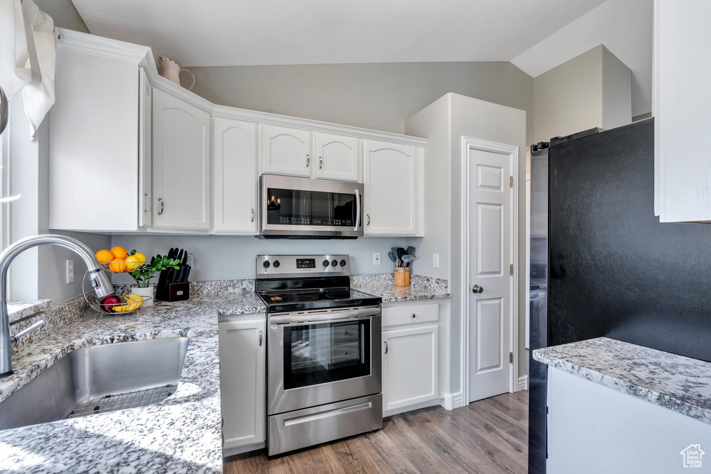 Kitchen featuring stainless steel appliances, white cabinets, vaulted ceiling, a sink, and wood finished floors