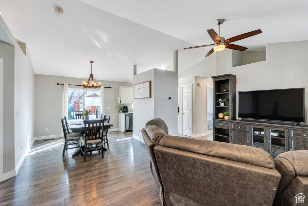 Living area featuring vaulted ceiling, dark wood finished floors, baseboards, and ceiling fan with notable chandelier