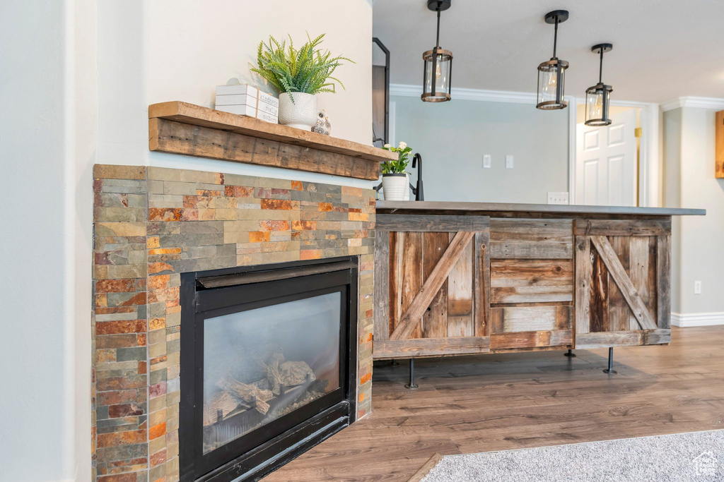 Bar featuring baseboards, a glass covered fireplace, ornamental molding, wood finished floors, and decorative light fixtures
