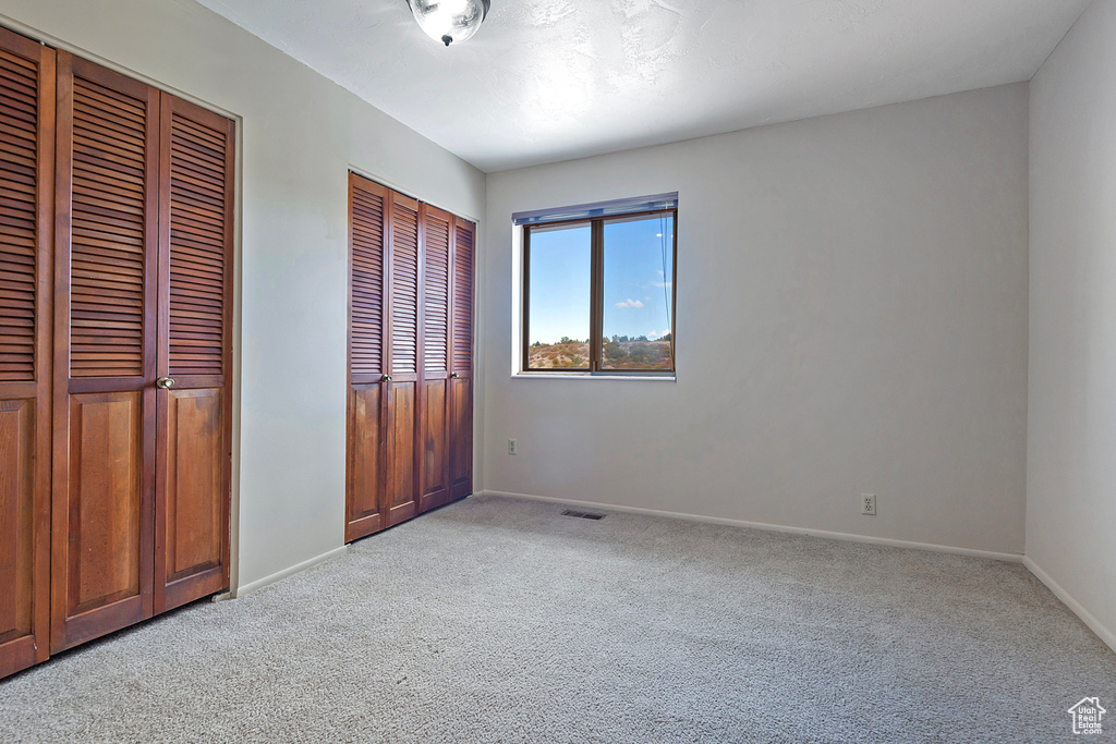 Unfurnished bedroom featuring baseboards, two closets, visible vents, and light colored carpet