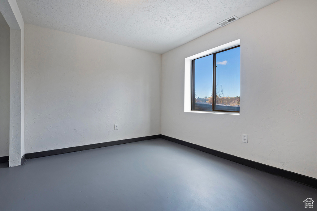 Empty room with concrete flooring, visible vents, a textured ceiling, and baseboards