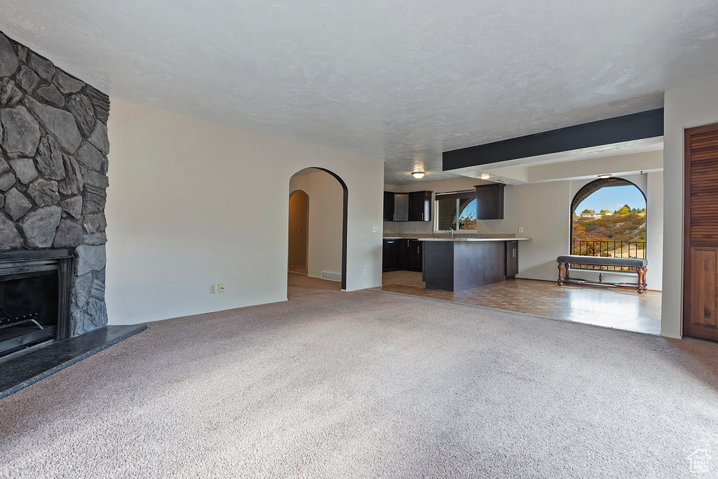 Unfurnished living room featuring arched walkways, light colored carpet, a fireplace, and a textured ceiling